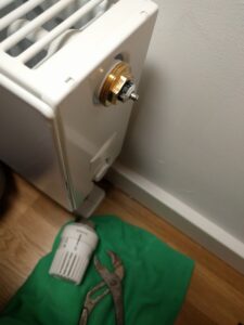 Blick von oben auf Heizkörper mit abmontiertem herkömmlichen Thermostat, Zange und Lappen