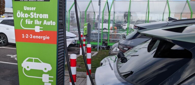 Elektroauto laden: Kosten im Vergleich – grüne Ladesäule links, rechts ladende und parkende Autos